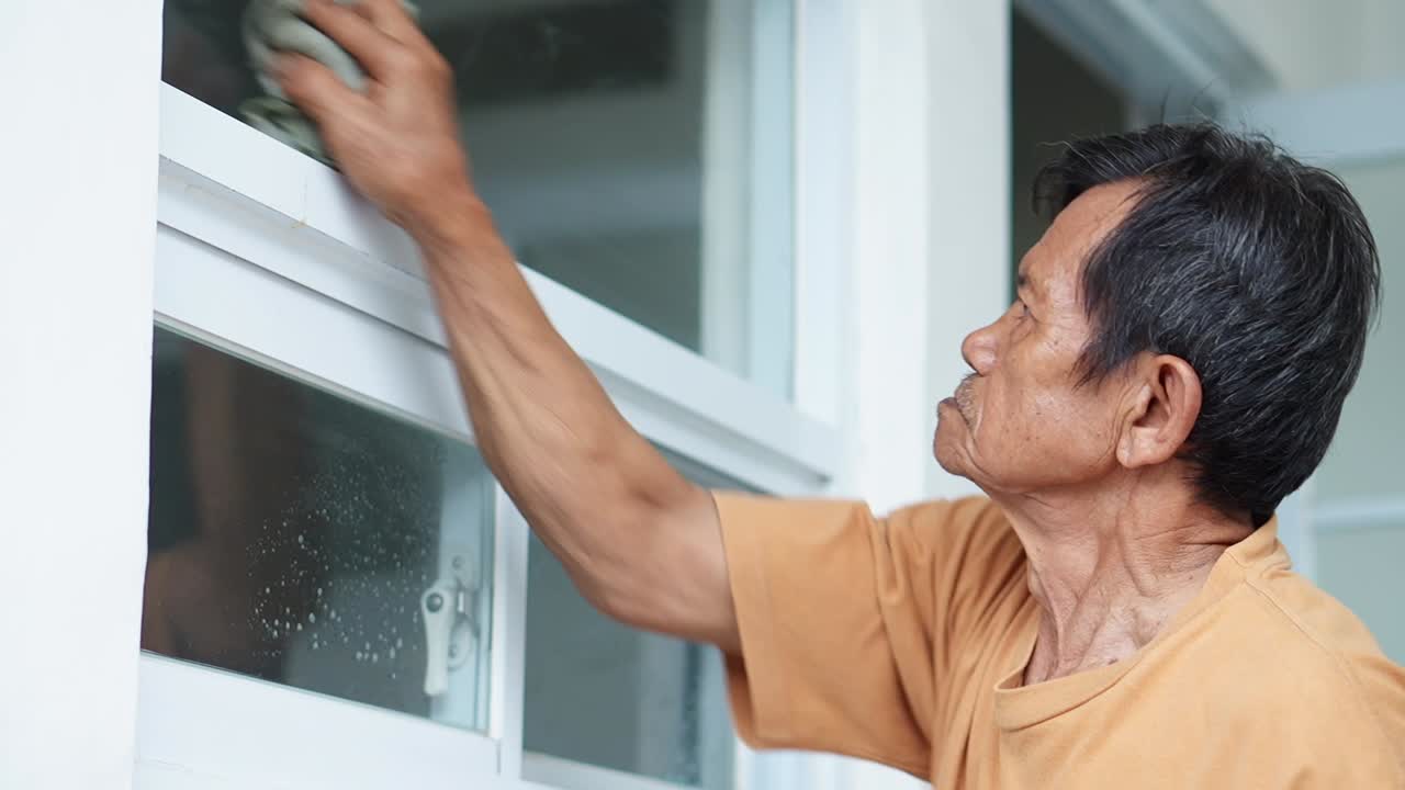 Elderly man diligently cleaning window with teacloth for maintaining pristine home environment