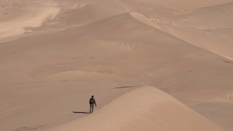 Man-walking-over-sand-dunes-on-a-sunny-day