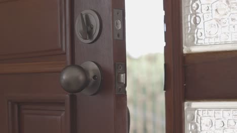 wooden door slowly closing but remaining slightly ajar, revealing a sunlit balcony and lush garden beyond, serene home transition shot for real estate ads