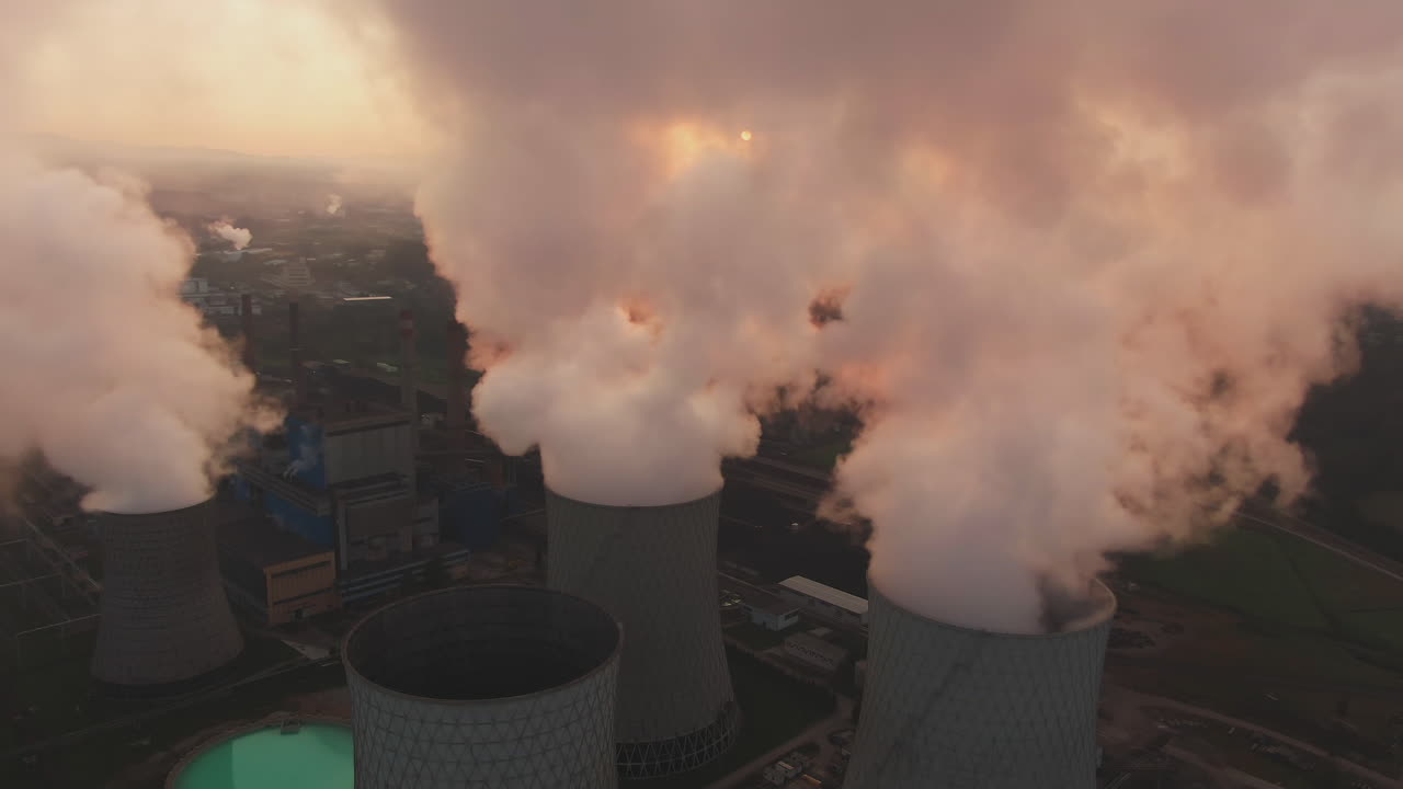 Aerial view of a power plant at sunset with smoke billowing from cooling towers