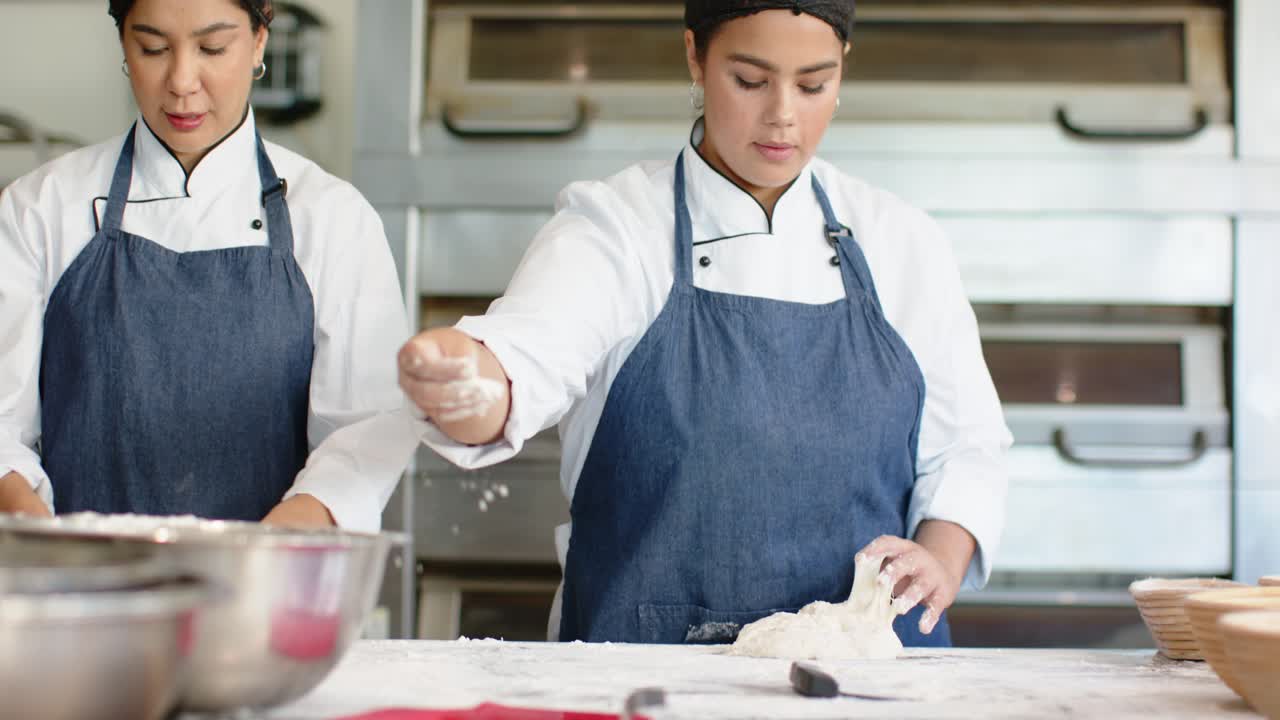 Female bakers in jackets right baker taking basket dusting flour kneading dough for oven at counter