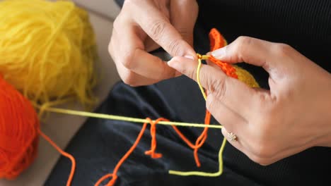 close-up of woman's hands crocheting with orange and yellow yarn