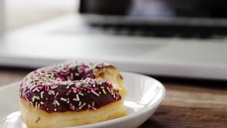 Half-eaten-chocolate-doughnut-with-sprinkles-on-wooden-table