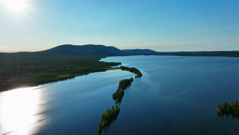 Drone-flying-backwards-over-lake-Pallasjarvi,-with-Lapland-mountain-background