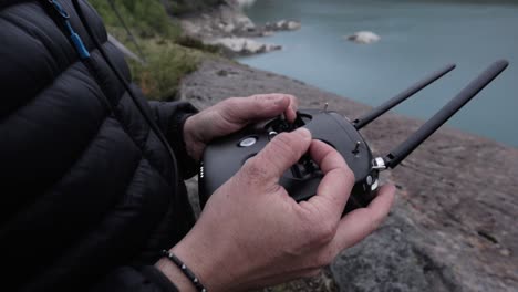 primer plano de piloto macho volando drone con controlador en la cima de la montaña con lago en segundo plano