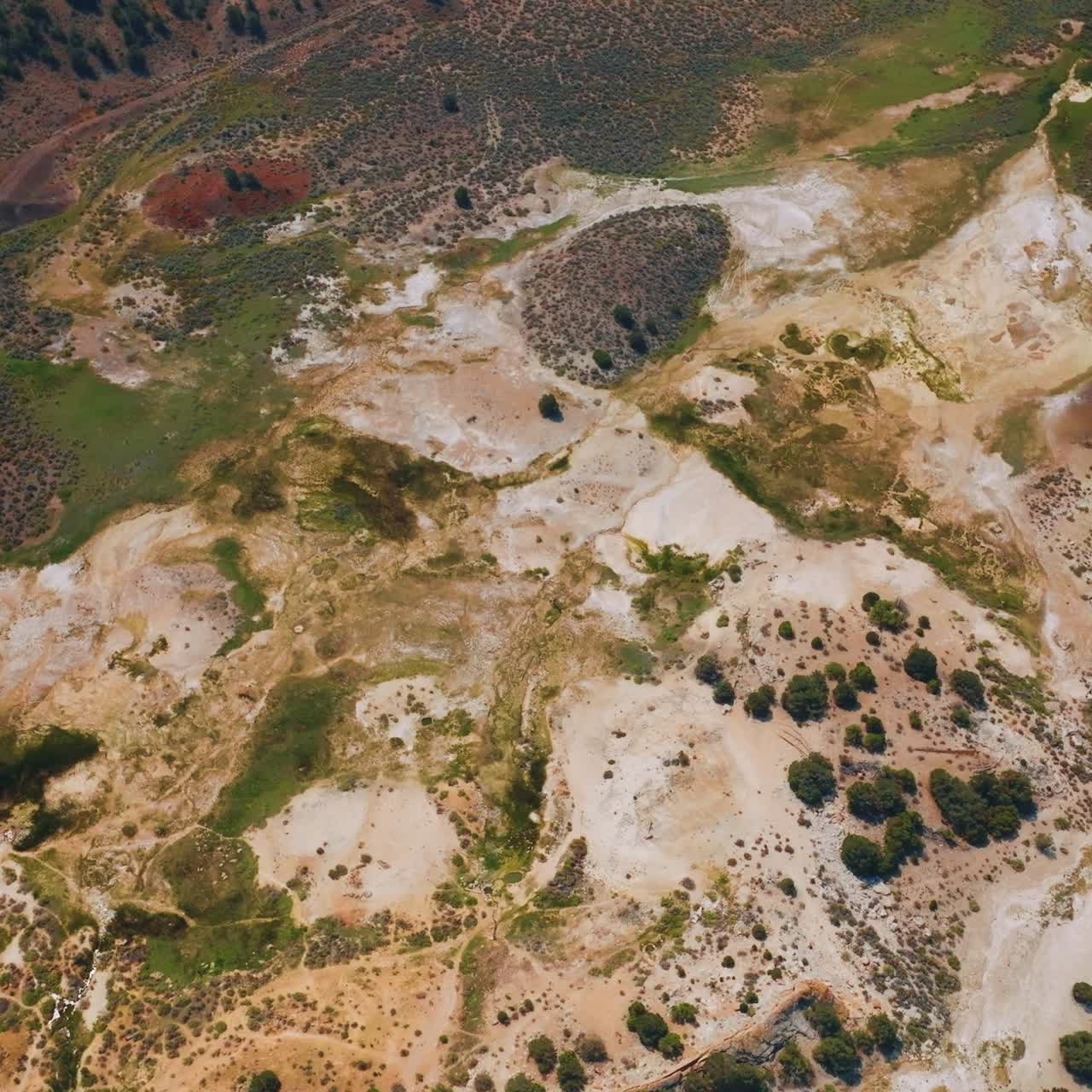 Flying over the multi-colored landscape of Travertine Hot Springs in California, USA. Rocky scenery with some vegetation growing on