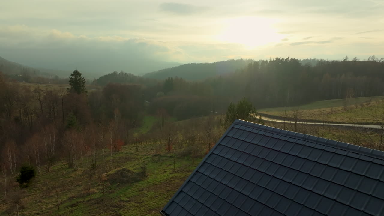 En hytte med udsigt over et frodigt landskab, med unge træer langs en nedadgående sti ind i et fredfyldt, skovklædt landskab under en blød, glødende himmel