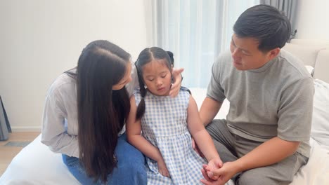 parents attentively care for their young daughter, checking her temperature in a softly lit bedroom