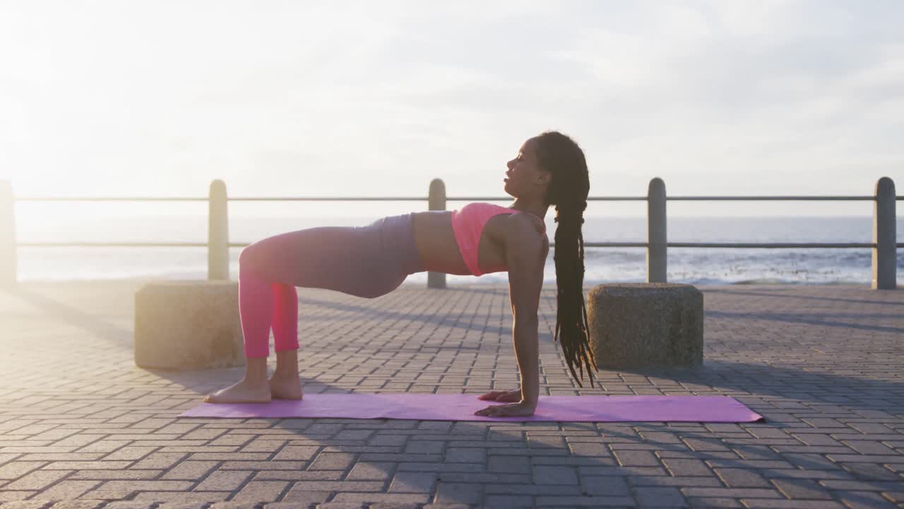African american woman in sportswear doing yoga on promenade by the sea