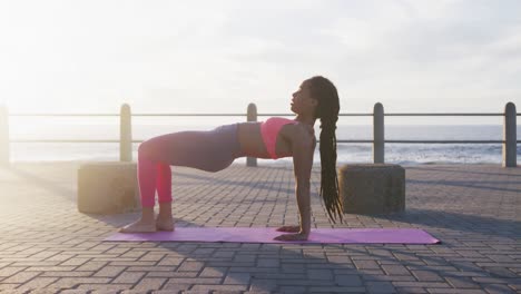 mujer afroamericana en ropa deportiva haciendo yoga en el paseo marítimo