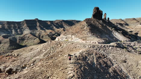 Aerial-tracking-on-long-haired-young-woman-heading-to-large-rock-formation-and-near-Medio-Almud-beach-in-Gran-Canaria-island-and-on-a-sunny-day