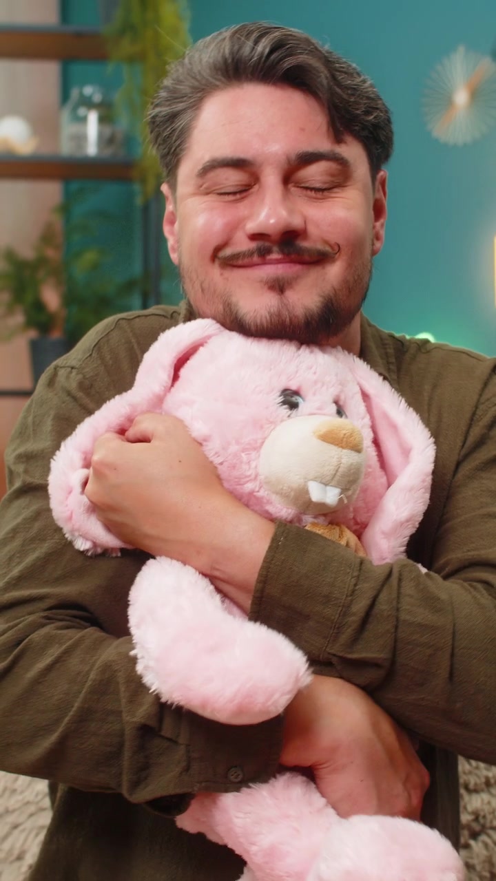 Uomo di mezza età che tiene in mano un coniglietto rosa, sorride tristemente, sente la mancanza del figlio, ricordando la tenera nostalgia del passato
