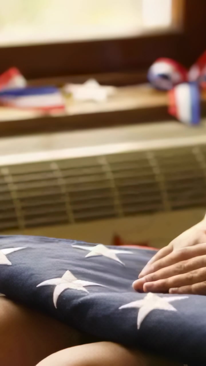 Vertical video: Placing adult hands smoothing folded US flag at window, paying respects