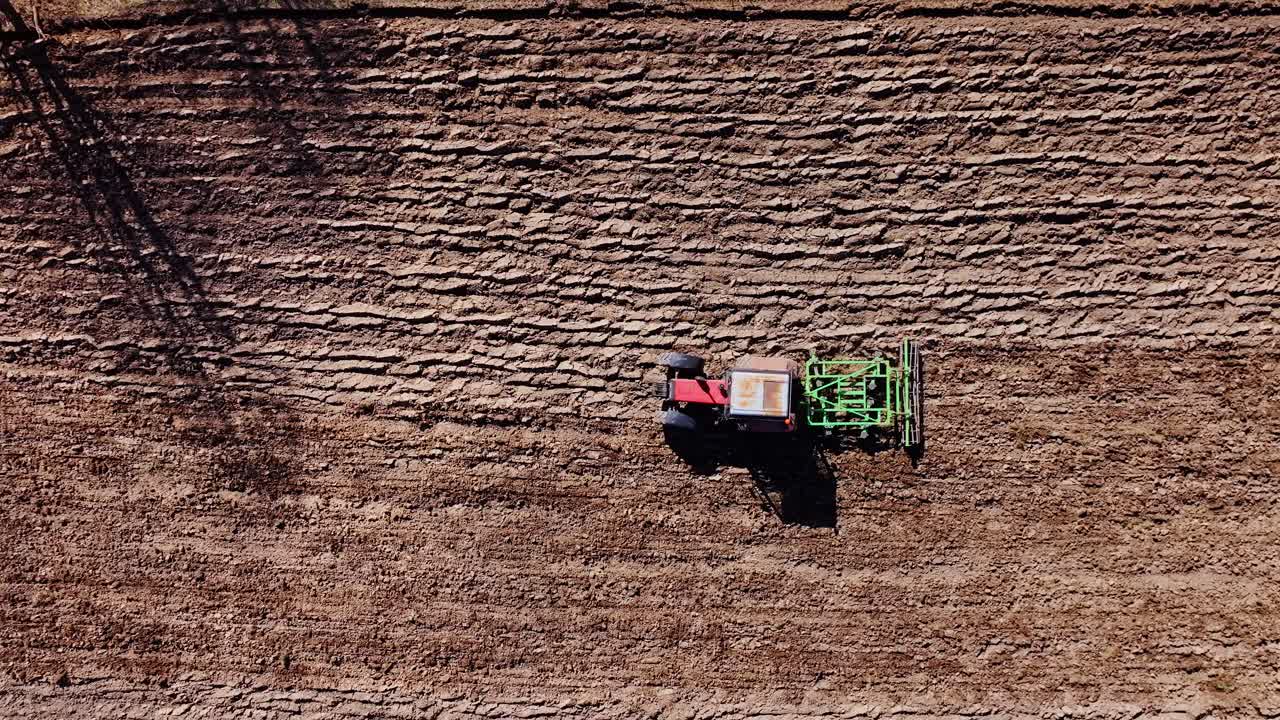 Top down drone view shows vintage red tractor cultivating brown Latvian soil