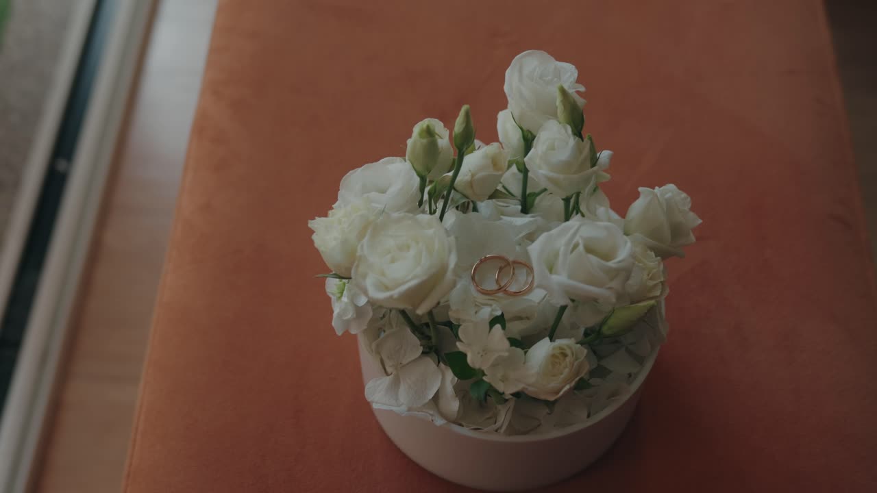 Two gold rings placed on white roses in round box