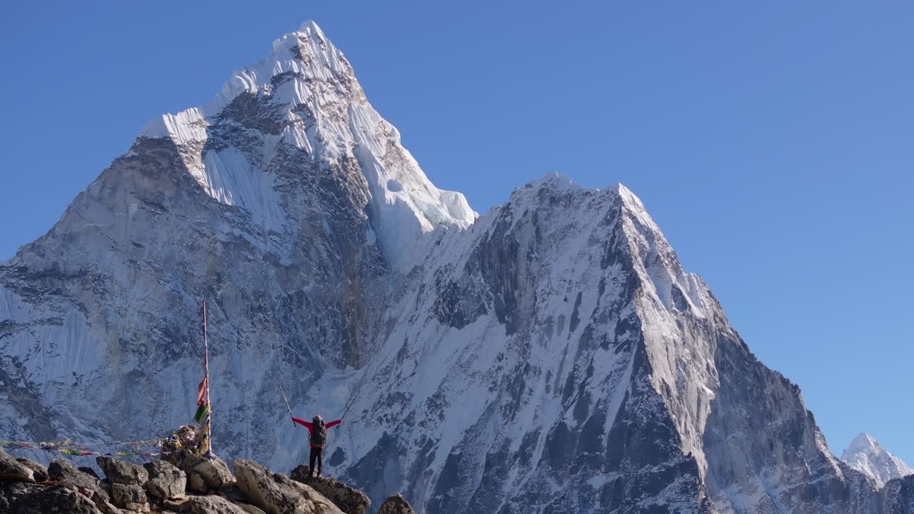 Filmato con drone di un escursionista che sale verso il Nangkartshang Peak sopra Dingboche, lungo il percorso del campo base dell'Everest in Nepal. L'Ama Dablam fa da sfondo mentre le bandiere di preghiera sventolano al vento.