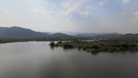 Aerial-View-of-the-Landscape-Over-a-Lake-with-Rising-Up-Drone-Shot-Revealing-the-Horizon-and-Mountains-in-the-Background