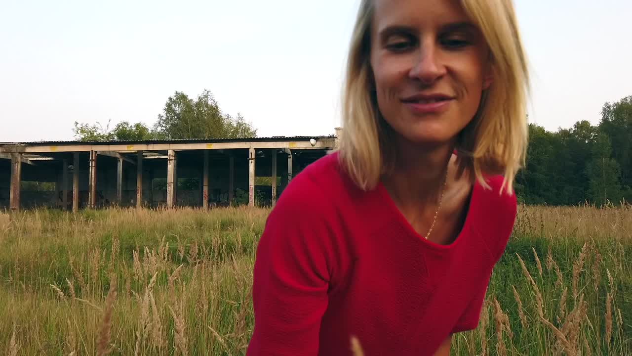 1 million $ slow motion cinematic shot of a girl in red dress picks flower in field. Shooting russians airfield. Gimbal foto video shoot on lost places in wild nature 1080, 24p by Philipp Marnitz