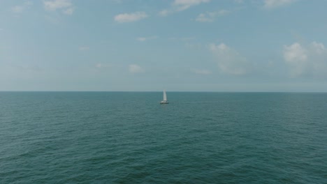 aerial establishing view of a white sailboat in the calm batltic sea, white sailing yacht in the middle of the boundless sea, sunny summer day, wide done shot moving forward