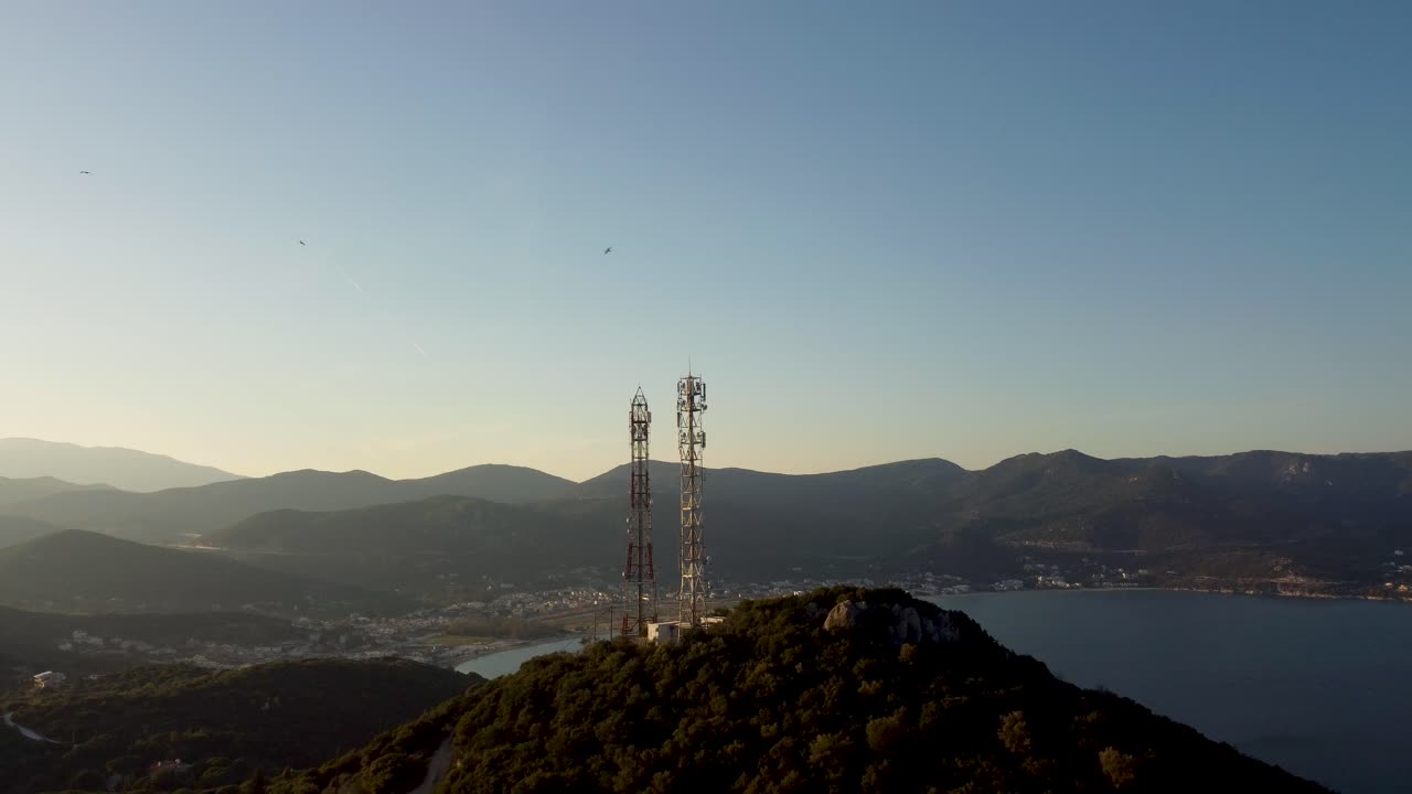 Aerial of telecommunications towers, antennas with small city in the background at golden hour. Network, connectivity.