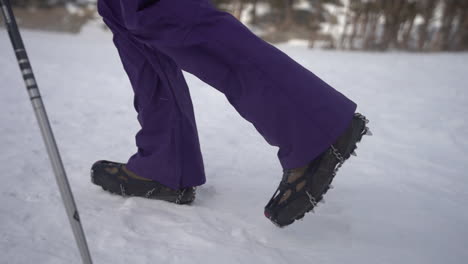 legs of hikers walking on snow with boots in icetrekkers chains, close up