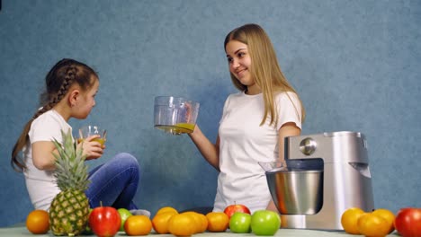 little girl and mother drinking freshly squeezed juice. organic fruit and a modern squeezer on the table. happy woman and daughter drink juice in turn.