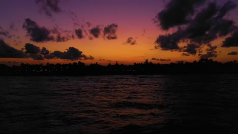 An-awesome-backwards-zoom-over-the-ocean-with-a-colorful-sunset-and-skyline-silhouette