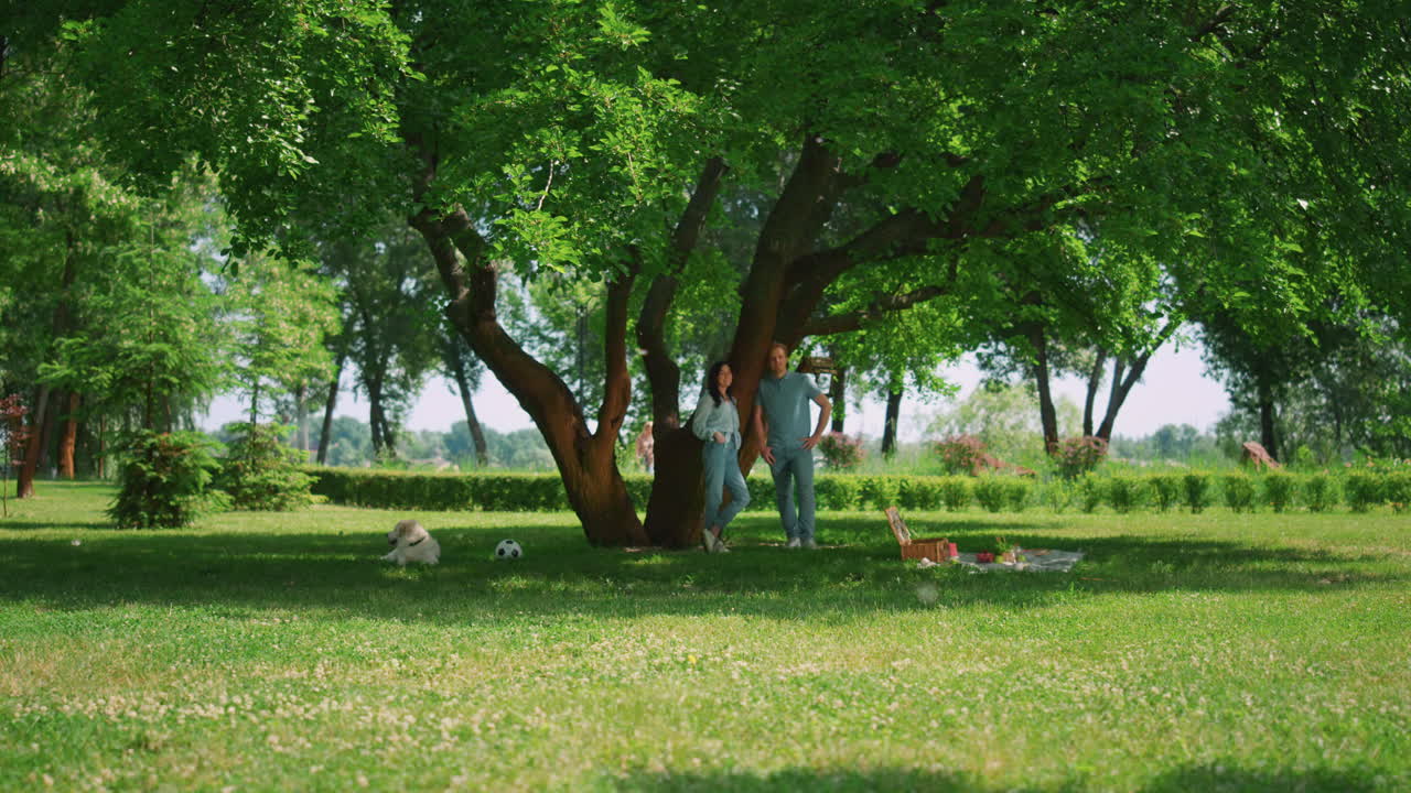 una pareja relajada de pie a la sombra de un árbol en el parque. un descanso familiar pacífico en un picnic.