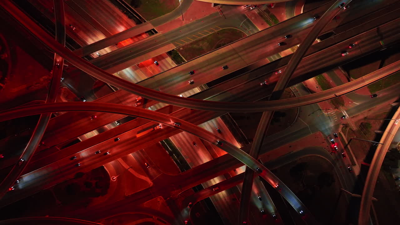 Descend over the interchange lit with red light. Night view on the intersection with hectic traffic from bird's eye perspective