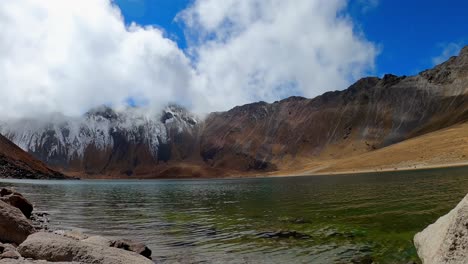 lapso de tiempo: impresionante escena de agua dulce clara lago nevado de toluca por la áspera cordillera escarpada con tenues cúmulos blancos y nubes estratos rodando en un día azul brillante cielo soleado