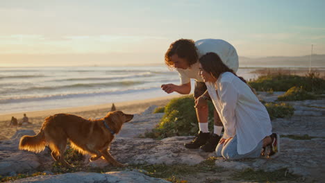 two teenagers talking to dog at evening beach. happy couple playing with pet