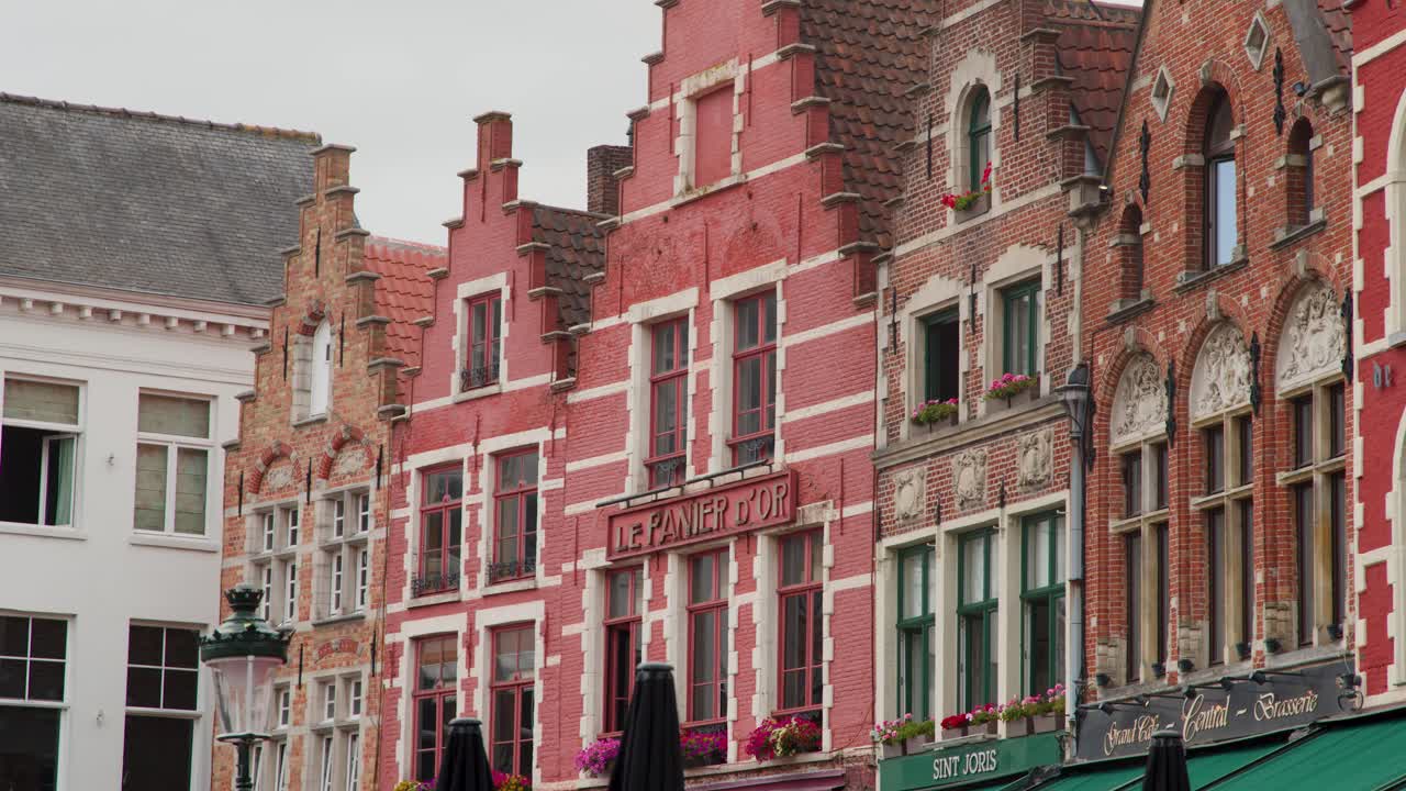 Camera slowly pans across ornate brick buildings with gabled roofs under overcast daylight in Bruges
