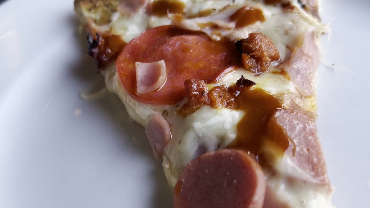 Handheld shot of pizza slice on a plate with ham, cheese and chorizo, close up
