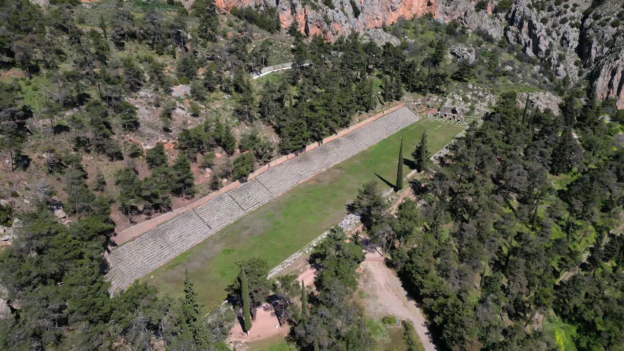 Ancient stadium at Delphi surrounded by forest and mountainous terrain, drone top