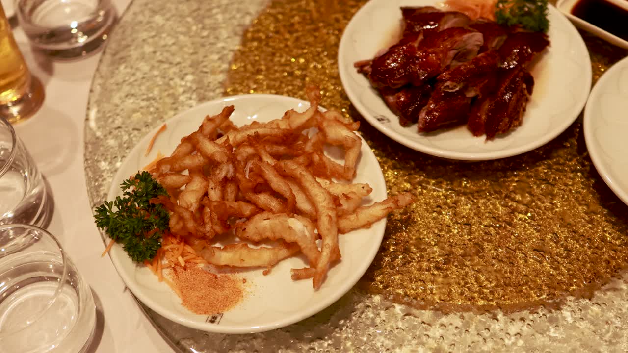 Aerial view of a spinning lazy Susan with Chinese dishes, including duck and fish, in a warmly lit restaurant setting