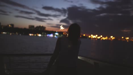 beautiful young woman dances on the deck of a ship with bengal lights at night. woman having fun time