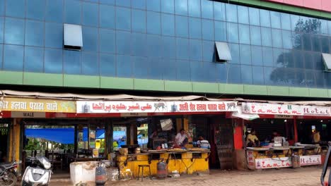 street view of a building with a reflective glass facade. the ground floor has several food stalls or small restaurants with signs in multiple languages