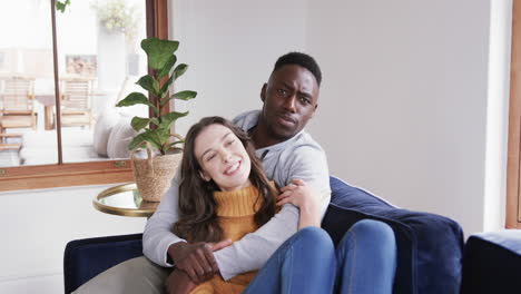 happy diverse couple sitting on sofa laughing and embracing in home,copy space