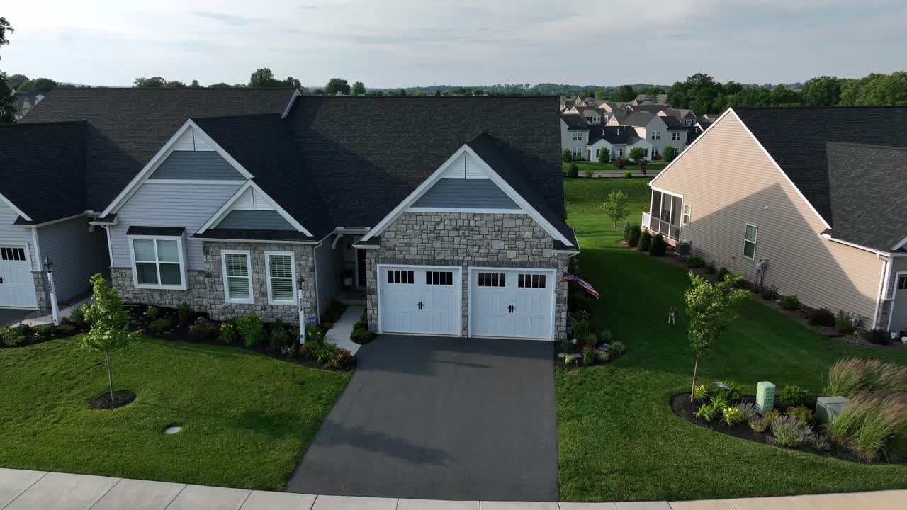 Aerial view of single family houses with double garage and flying American flag in neighborhood. Barking dog on grass of front yard. Sunset time. Suburb housing area in U.S