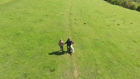 Toma-Aérea-De-La-Pareja-Madura-Y-El-Perro-A-Caminar-En-El-Campo