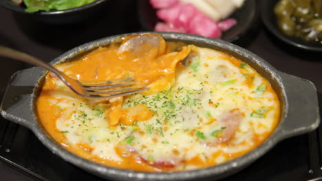 Female&#039;s hand picks up melted cheese from potato gratin in metal bowl with fork in korean fusion restaurant - close-up slow motion