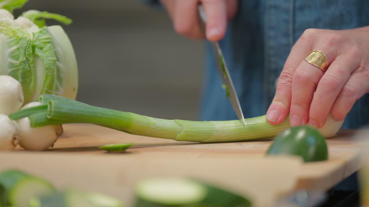 Detail of a chef's hand slicing green onions and leeks for a meal