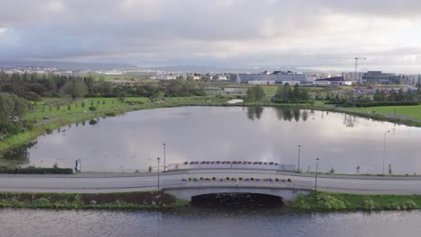 Idyllic-bridge-crossing-lake-Tjörnin-in-capital-of-Iceland,-aerial