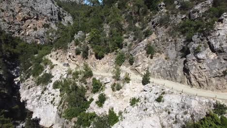 Aerial-following-shot-of-a-car-driving-on-a-narrow-mountainous-gravel-road-along-the-edge-of-a-cliff