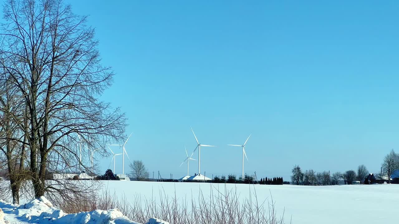 Moderní větrné turbíny s točícími se lopatkami generující čistou, obnovitelnou energii na rozlehlém, zasněženém poli během slunečného zimního dne, propagující udržitelnou technologii a výrobu energie.