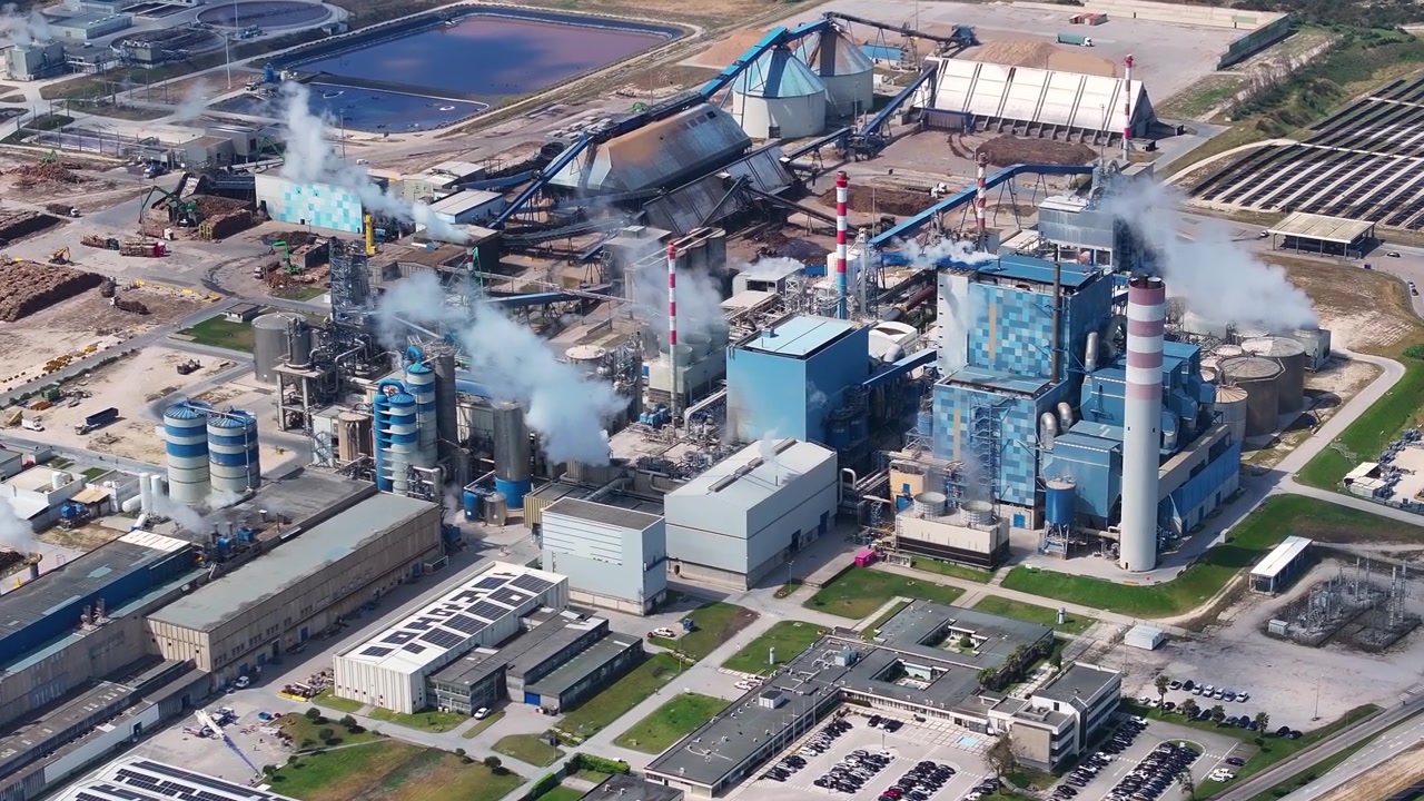Aerial perspective of a large pulp mill and biomass power plant processing wood into cellulose. Industrial chimneys releasing steam