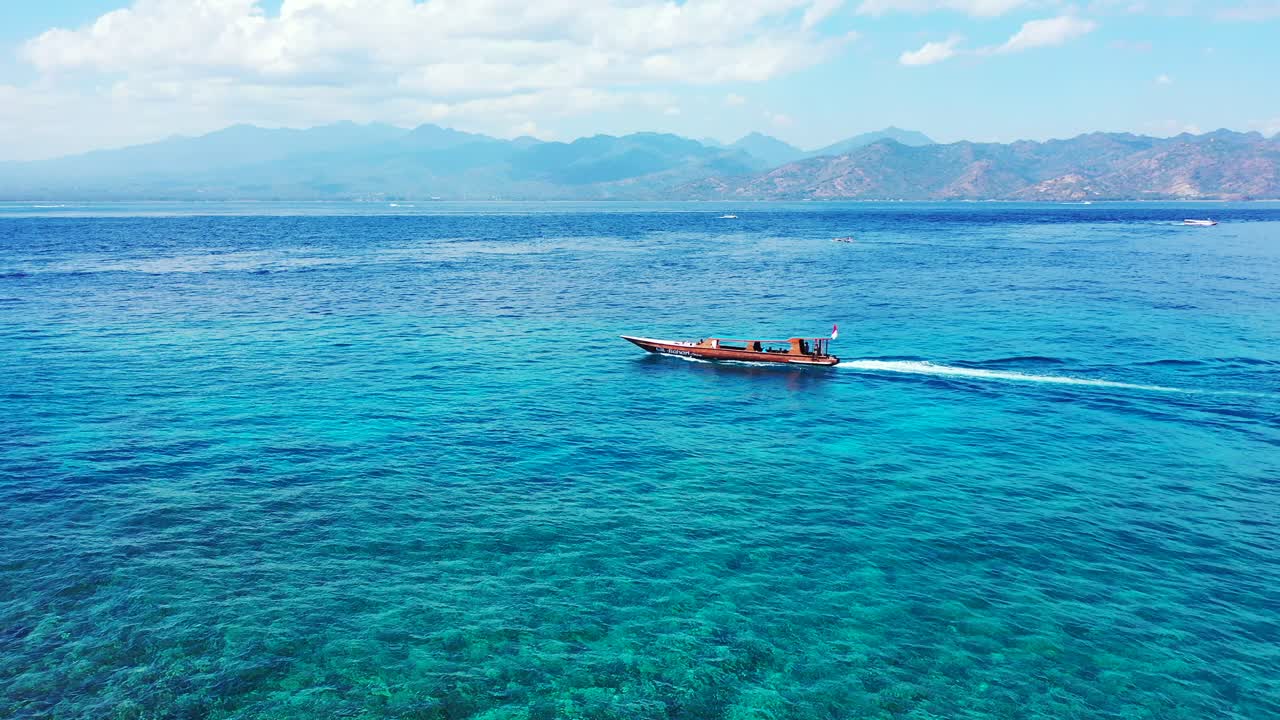 Long tail boat sailing across turquoise lagoon toward deep blue sea and tropical islands with high mountains under cloudy sky in Bali