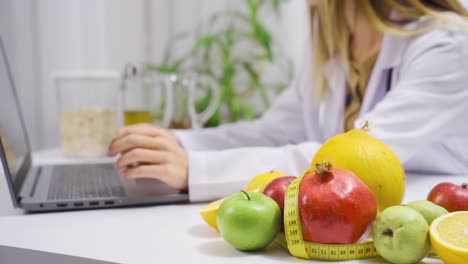 Mujer-Nutricionista-Que-Trabaja-Con-Una-Computadora-Portátil-En-El-Hospital.-Frutas-Y-Verduras-En-La-Mesa.