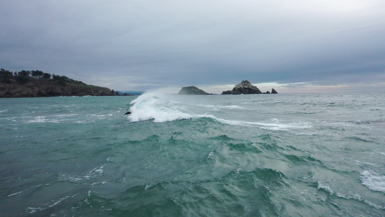 Drone flight over the rocky, windy coast of Mendocino, California with waves crashing along the beach on a cold day