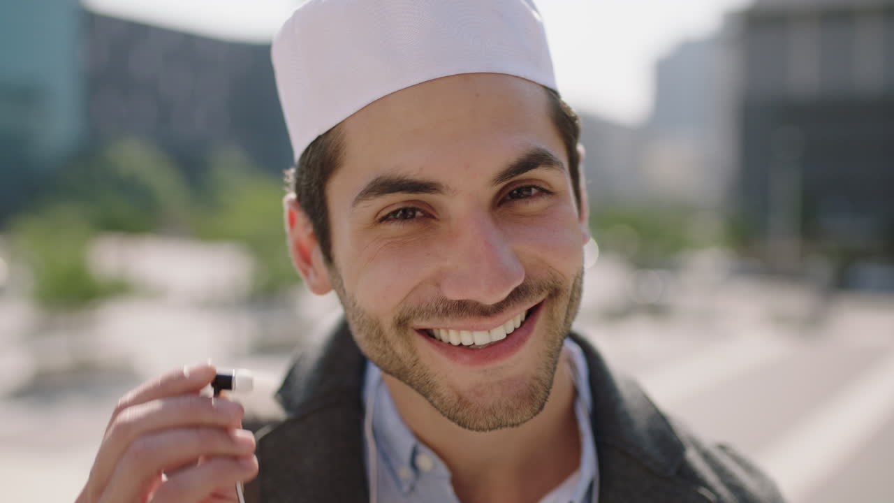retrato de un atractivo joven árabe de oriente medio escuchando música quita los auriculares sonriendo feliz a la cámara disfrutando del estilo de vida urbano usando kufi